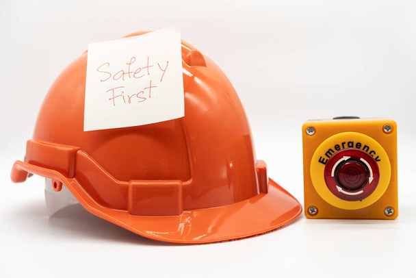Oranssi turvahattu ja viesti Turvallisuus Ensimmäinen ja Emergency Stop Button eristetty valkoisella taustalla. Turvallisuus ensimmäinen käsite. - Valokuva, kuva