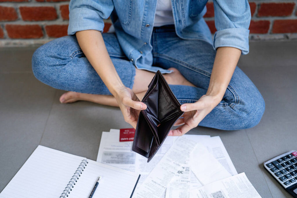Top view of empty wallet. Stressed Asian woman sitting on floor calculating expenses on invoice or bill. Concept of bankruptcy. - Photo, Image