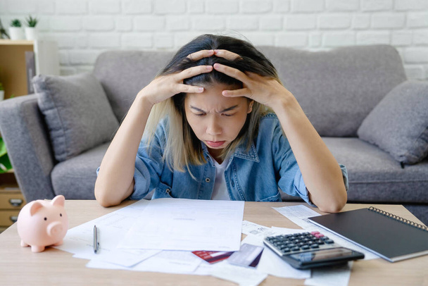 Asian female sitting expression face stressed by calculate expense on table from invoice or bill. She had financial and cost of living problems. - Photo, Image