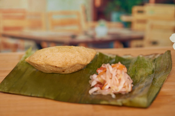 Delicia culinaria centroamericana de El Salvador llamada Pastelito mader de carne en un restaurante sobre una mesa de madera servida con curtido. - Foto, imagen