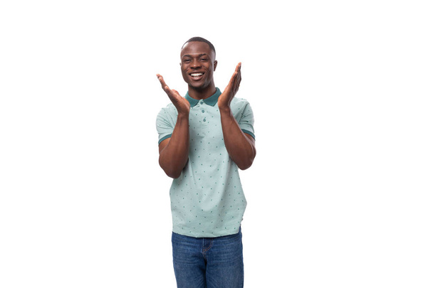 молодой дружелюбный африканский парень с короткой стрижкой, одетый в мятную футболку с воротником, улыбающийся. - Фото, изображение