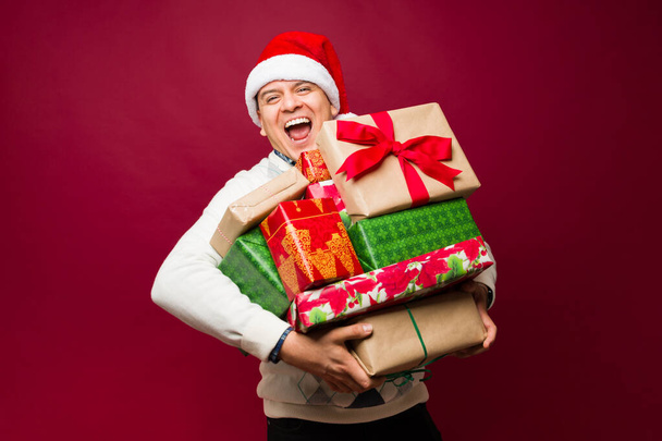 Latinalainen mies nauraa hauskaa kantaen paljon kauniita lahjoja ja lahjoja antaa joulun aikana ja hymyillen - Valokuva, kuva