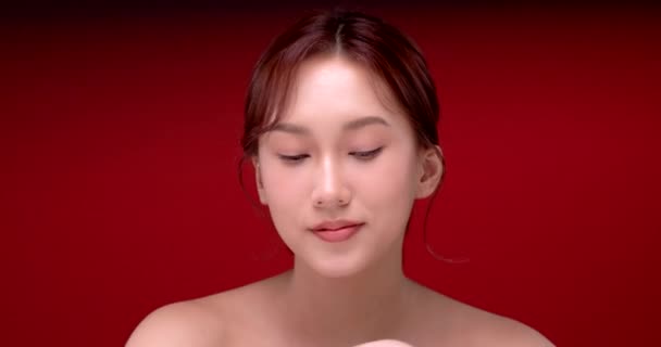 Schöne junge asiatische Frau mit sauberer, frischer Haut auf rotem Hintergrund, Gesichtspflege, Gesichtsbehandlung, Kosmetologie, Schönheit und Wellness, asiatische Frauenporträt. - Filmmaterial, Video