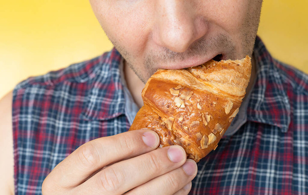 Un hombre irreconocible comiendo un croissant. Primer plano de un hombre comiendo un croissant. - Foto, Imagen