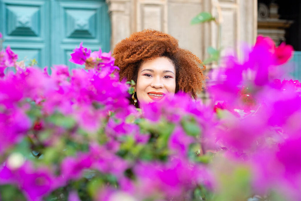 Egy mosolygó vörös hajú nő portréja az orgona és a zöld levelű vörös virágok között. Magabiztos és nyugodt személy. - Fotó, kép
