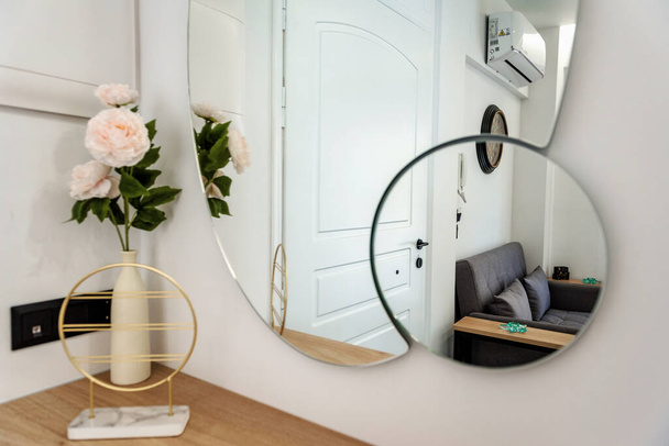Detalhe interior intrigante: Mesa adornada com um vaso de flores, parede espelhada refletindo um sofá, criando um ambiente caseiro cativante e elegante. - Foto, Imagem