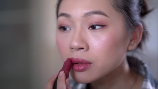 Jovem atraente Asiático fêmea em roupas casuais aplicando batom brilhante enquanto olha para o espelho - Filmagem, Vídeo