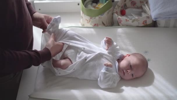 Van boven van gewas onherkenbare vader kleden charmante pasgeboren baby thuis in het zonlicht - Video