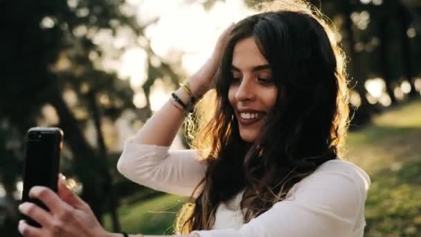 Jeune jolie femme prenant selfie avec smartphone dans un parc verdoyant - Séquence, vidéo