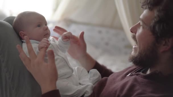 Oldalnézetben termés apa beszél bájos kis gyermek és grimaszolás, miközben nézik egymást a hálószobában - Felvétel, videó