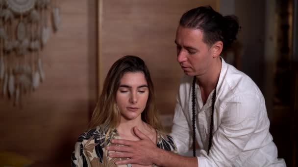 Zen-Lehrer in weißer Kleidung berührt Brust einer Frau mit gekreuzten Beinen während Yoga-Praxis in der Nähe des Schüsselgong - Filmmaterial, Video