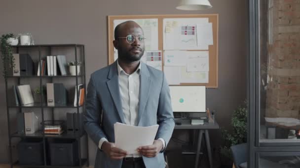 Slowmo πορτρέτο του αρσενικού Αφροαμερικανού εργαζομένου που κατέχει έγγραφα και βρίσκεται στο γραφείο την ημέρα - Πλάνα, βίντεο
