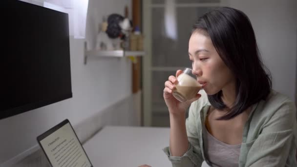 Zijaanzicht van jonge etnische vrouwelijke blogger aan het bureau met netbook en koffie op het scherm in huis kamer  - Video