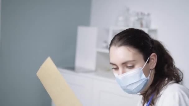 mladá žena lékař nošení bílý kabát psaní poznámky na pracovišti - Záběry, video