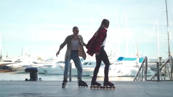 Cuerpo completo de jóvenes amigos positivos tomados de la mano en patines disfrutando de un agradable tiempo libre juntos en primera línea de mar al atardecer - Metraje, vídeo