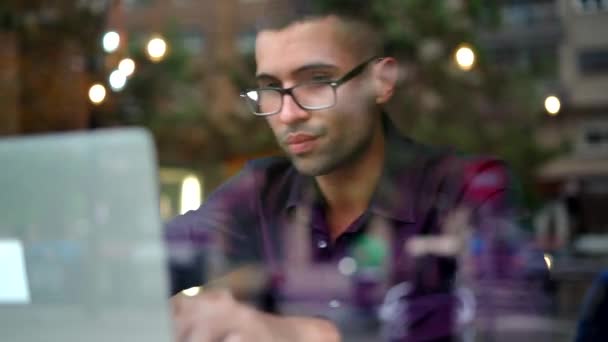 Komoly spanyol férfi menedzser lila ingben és szemüvegben gépel a netbook billentyűzeten, miközben az ablak mögött ül és a projekten dolgozik a kávézóban. - Felvétel, videó
