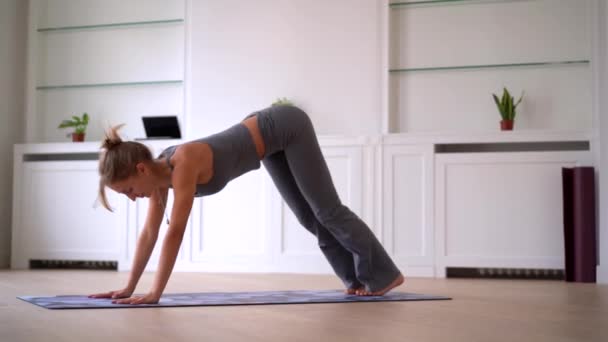 Vista lateral de delgada hembra haciendo yoga sobre estera en habitación espaciosa en casa - Metraje, vídeo