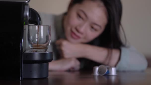 Genç ve etnik bir kadın, mutfak mutfağında köpüklü sıcak içecek dolduran kahve makinesine yaslanıyor. - Video, Çekim