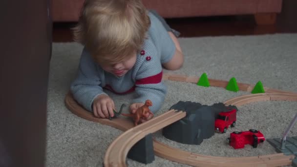 Göndör hajú kisfiú játszik dinoszauruszok szőnyegen otthon - Felvétel, videó