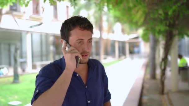 Fahndungsfoto eines männlichen Immobilienmaklers, der im Park eines modernen Bürogebäudes der Immobilienfirma ein Arbeitsgespräch auf dem Handy führt - Filmmaterial, Video