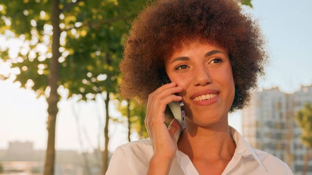 Close up smiling African American happy ethnic girl businesswoman walking in sun sunshine city remote talk talking mobile phone smile end finish business call woman employer lady walk going outdoors - Foto, afbeelding