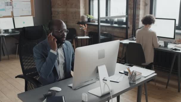 Yüksek açılı Afrikalı Amerikalı erkek ofis çalışanı bilgisayarla masada oturup müşteriyle görüntülü konuşma yapıyor. - Video, Çekim