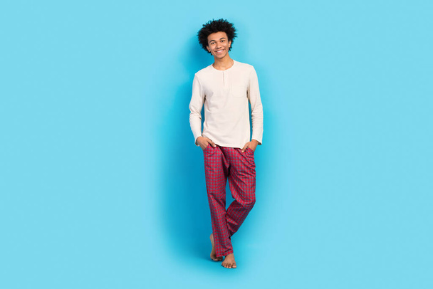 Full size photo of cute young guy posing hands pockets shopping wear trendy white pajama outfit isolated on blue color background. - Photo, Image