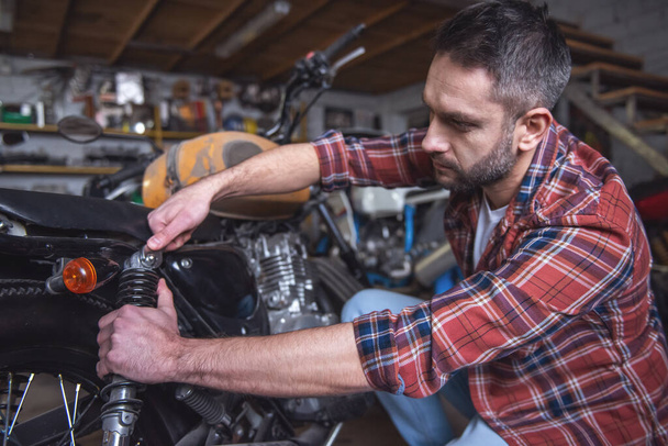 Красавчик ремонтирует мотоцикл в мастерской.
 - Фото, изображение
