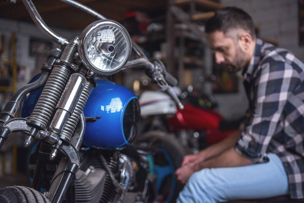Красивий чоловік ремонтує мотоцикл у ремонтному магазині
 - Фото, зображення