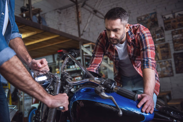 Beaux gars examinent une moto avant de la réparer dans l'atelier de réparation
 - Photo, image