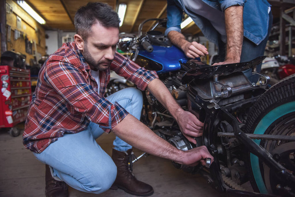 Beaux gars sont la réparation d'une moto dans l'atelier de réparation
 - Photo, image