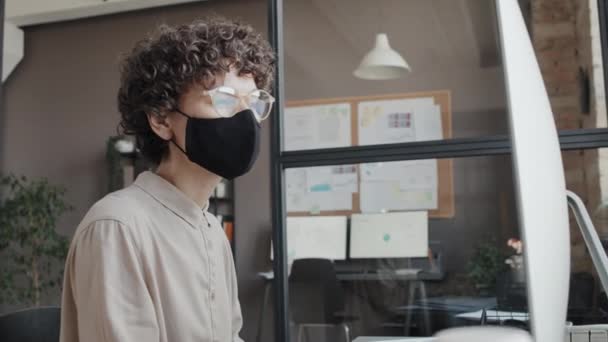 若い白人女性がマスクを着用し,昼間にオフィスでコンピュータで作業する中型ショット - 映像、動画