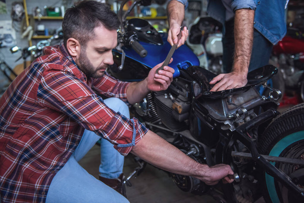 Красивые парни ремонтируют мотоцикл в ремонтной мастерской
 - Фото, изображение