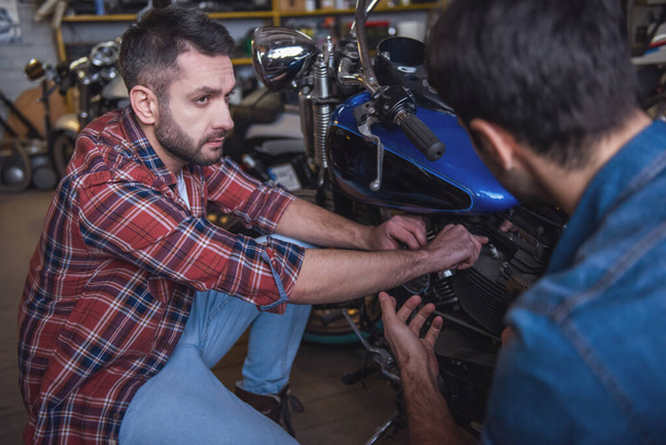 gutaussehende Kerle unterhalten sich beim Reparieren eines Motorrads in der Werkstatt - Foto, Bild
