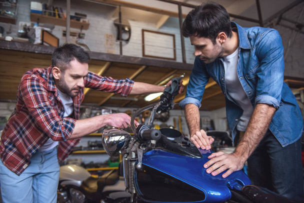 Beaux gars sont la réparation d'une moto dans l'atelier de réparation
 - Photo, image