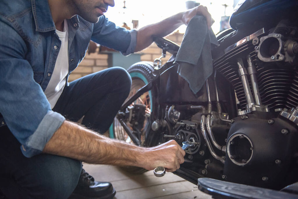 Привлекательный мужчина ремонтирует мотоцикл в мастерской
 - Фото, изображение