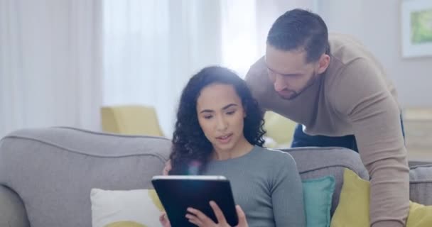 Happy couple, talking and bonding on tablet on sofa for internet browsing, social media or blog reading in house. Smile, woman or talking biracial man on digital technology in home for web research. - Footage, Video