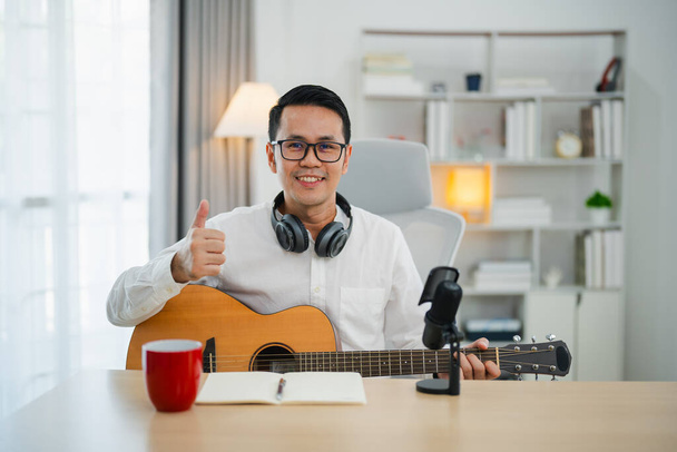 Asiatico uomo youtuber live streaming perfomance suonare la chitarra e cantare una canzone. Uomo asiatico che insegna chitarra e canto online. Musicista che registra musica con laptop e suona la chitarra acustica. - Foto, immagini