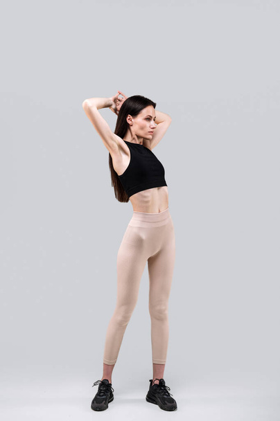 Вертикальний вигляд стрункої жінки в активному вбранні, що стоїть ізольовано на сірому фоні. Жінки в спортивному одязі відвідують фітнес-центр для тренувань з відновлення. Концепція фізичної активності для нарощування м'язів - Фото, зображення
