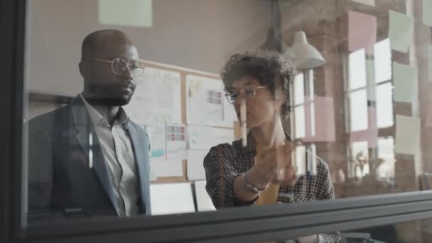 Keskikokoinen laukaus mies Afrikkalainen Amerikan ja naisen Valkoihoinen toimistopäälliköiden katselee seinään tahmea muistiinpanoja - Materiaali, video