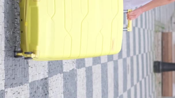 Een meisje loopt over de zebrapad met bagage. Concept van reizen, levensstijl. Langzame beweging. Verticale video. - Video
