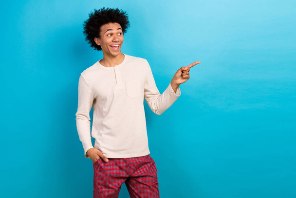 Photo portrait of attractive young man point excited empty space dressed stylish white pajama clothes isolated on blue color background. - 写真・画像