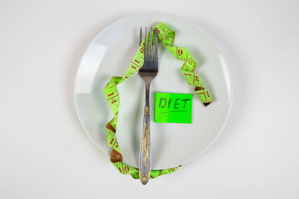 tenedor y cinta métrica en un plato como símbolo de alimentación saludable. - Foto, Imagen