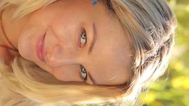 Egy gyönyörű szőke nő portréja, aki a kamerába néz és mosolyog. Egy nő nyugszik a természetben. Függőleges videó. - Felvétel, videó