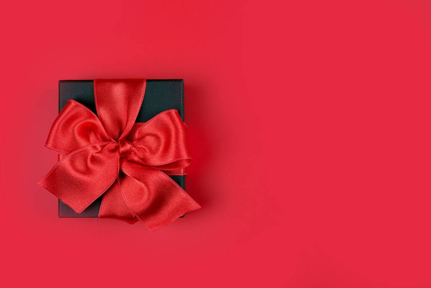Musta lahjapakkaus, jossa punainen nauha punaisella taustalla ja tilaa tekstille - Valokuva, kuva