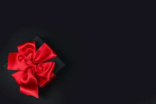 Schwarze Geschenkbox mit roter Schleife auf rotem Hintergrund mit Platz für Text - Foto, Bild