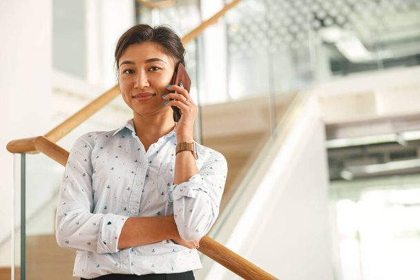 Attractive businesswoman talking phone with client while standing in office on stairs  - Photo, Image