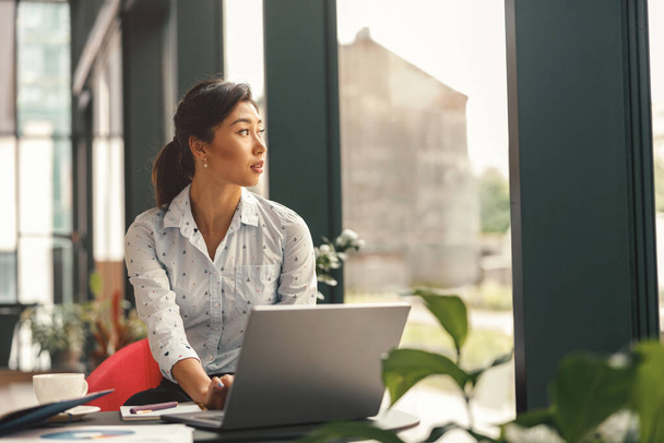Keskittynyt tyylikäs liiketoiminnan nainen työskentelee kannettavan tietokoneen istuu työpöydän taustalla - Valokuva, kuva
