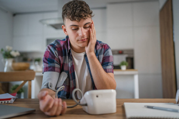 Один подросток мужчина белый подросток молодой мужчина сидит за столом проверить измерить кровяное давление на дому реального человека концепции здравоохранения - Фото, изображение