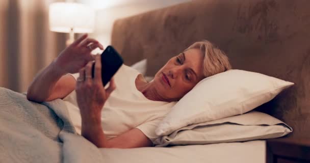 Éjszaka, olvasás és egy nő egy telefon az ágyban a közösségi média, chat vagy internet. Ház, weboldal és egy idősebb személy gépel egy mobil alkalmazáson kapcsolattartás, kommunikáció vagy értesítés céljából a hálószobában. - Felvétel, videó